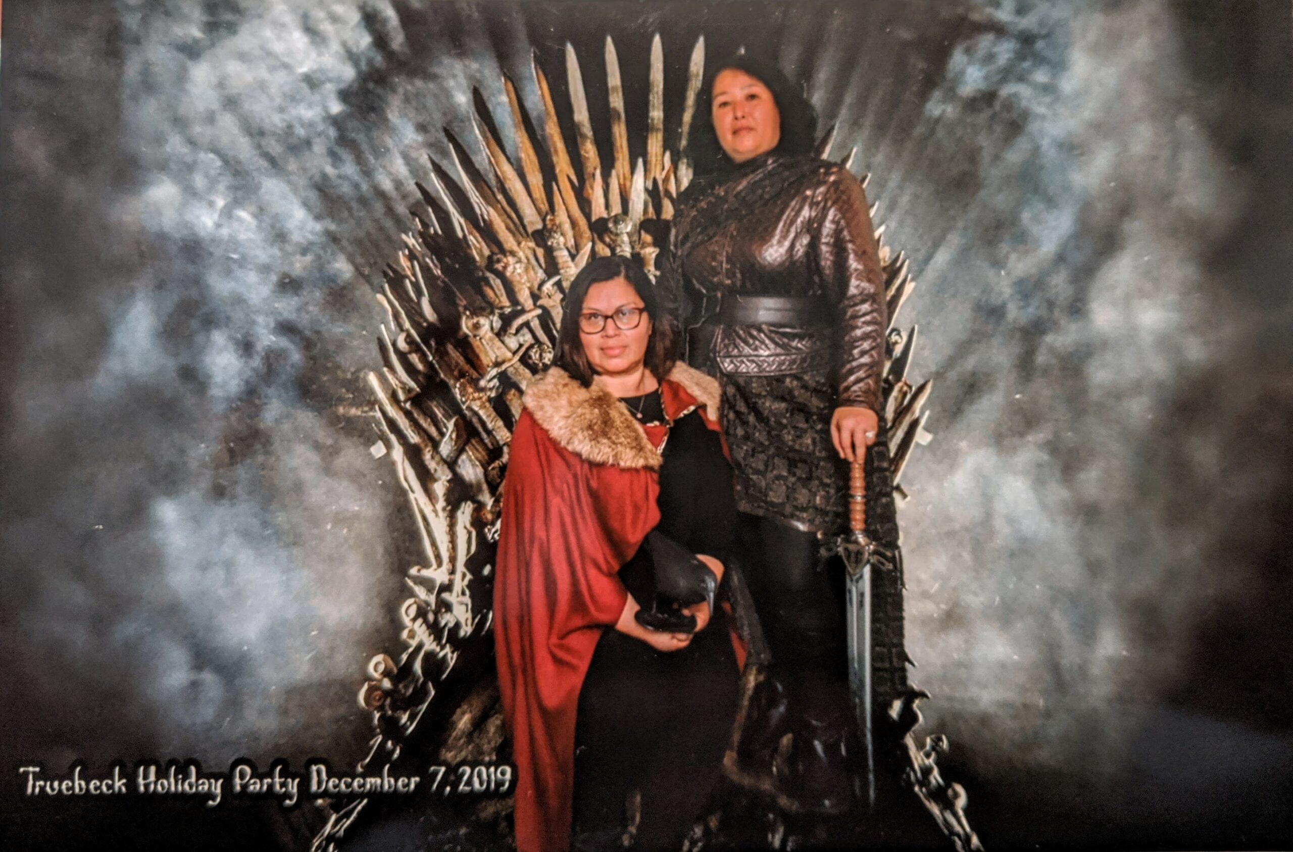A woman and man are posing for a picture in front of the iron throne.