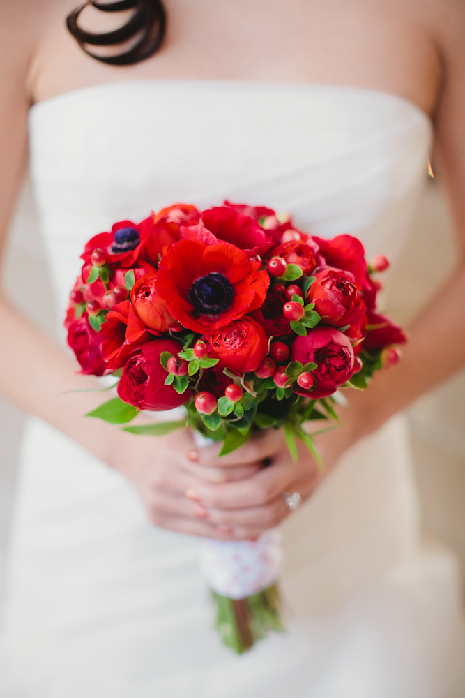 A bride holding her bouquet of red flowers.