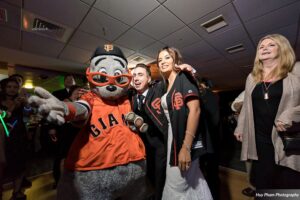 A couple posing with an animal dressed as a baseball player.