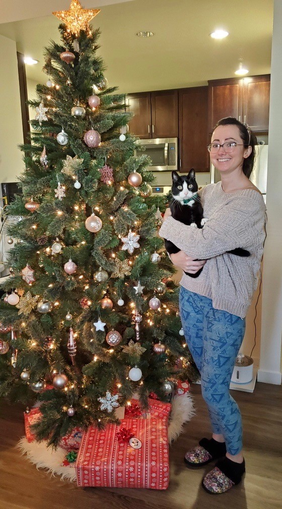 A woman holding a cat in front of a christmas tree.