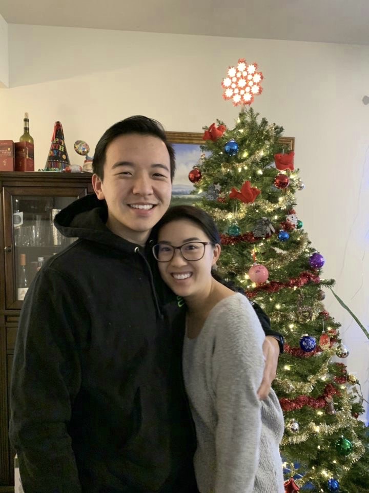 A man and woman standing in front of a christmas tree.