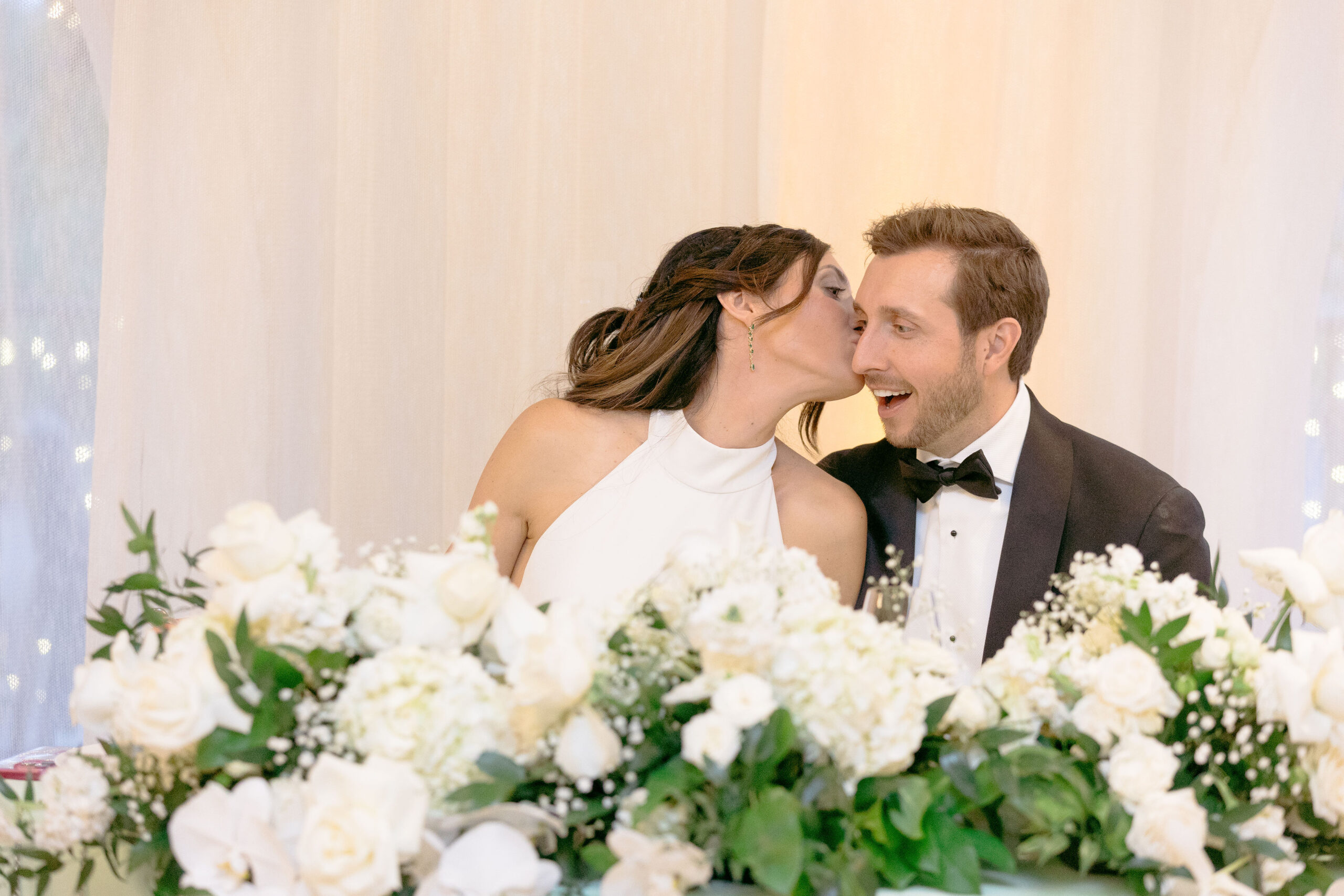 A bride and groom kissing in front of white flowers.