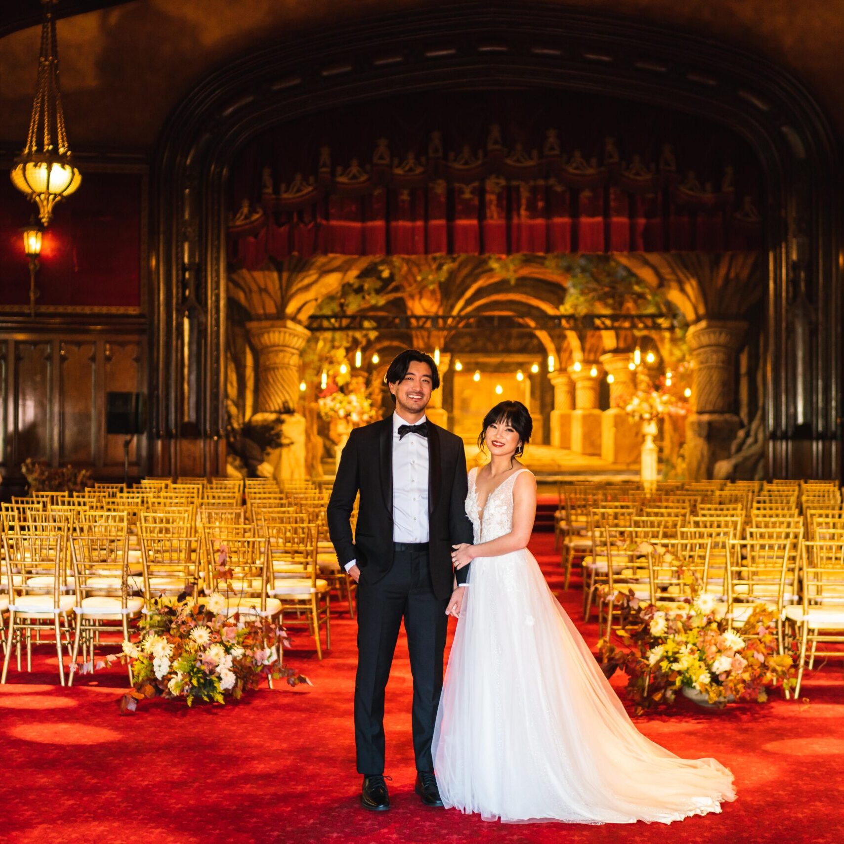 A bride and groom pose for a picture in front of the golden stage.