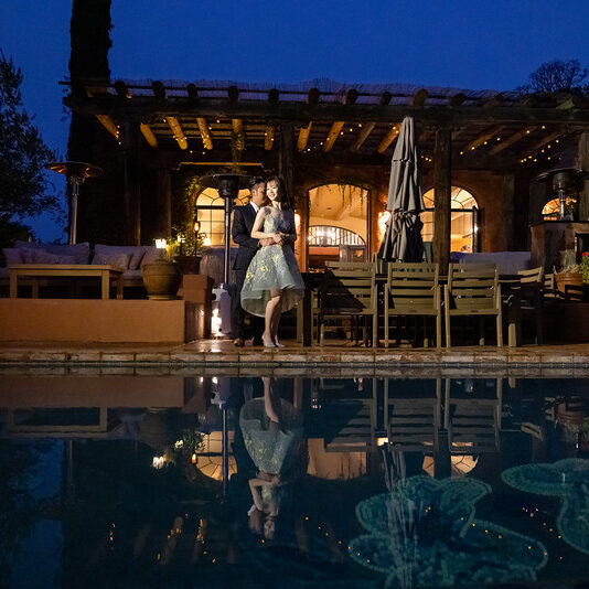 A couple standing next to the pool at night.