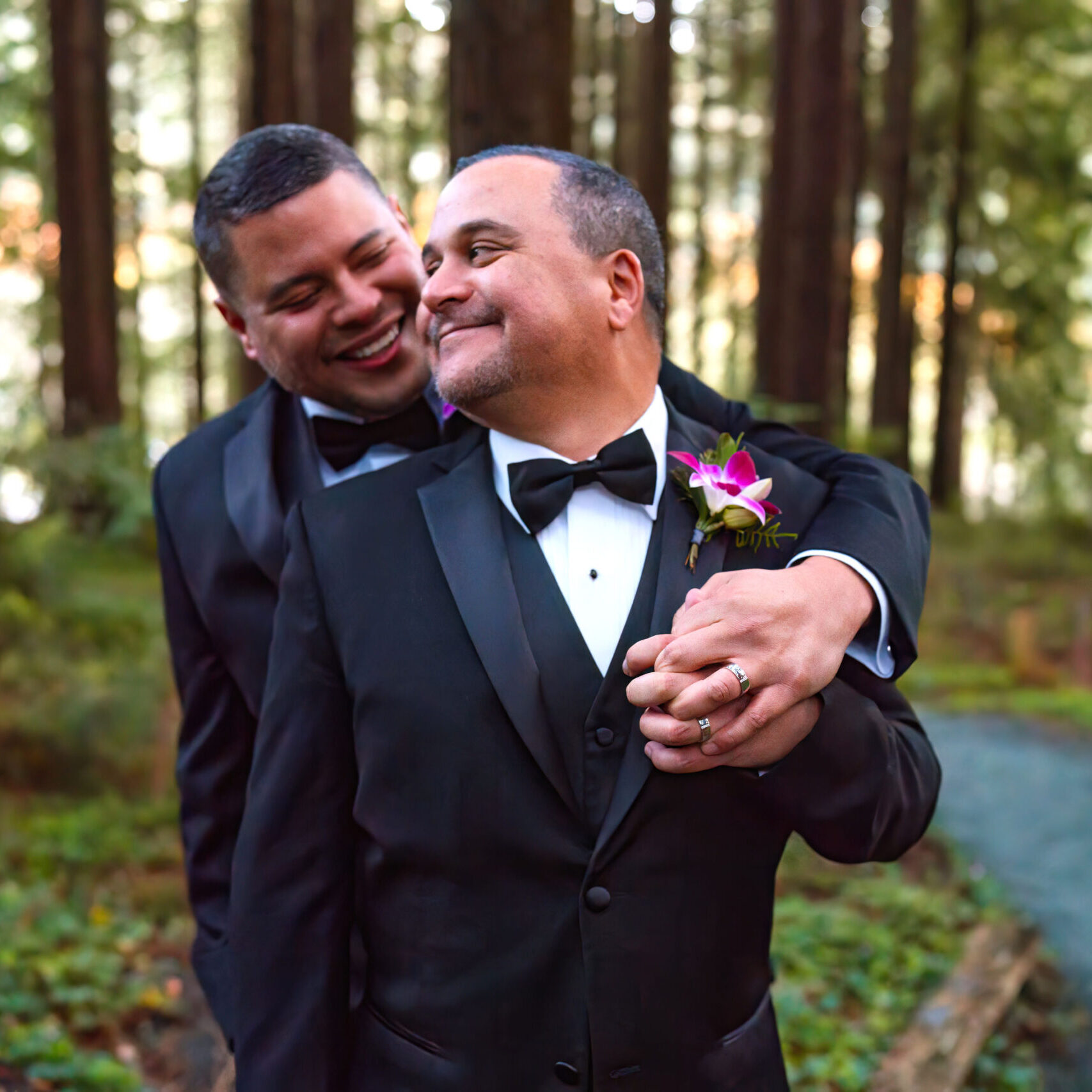 Two men in tuxedos pose for a picture.