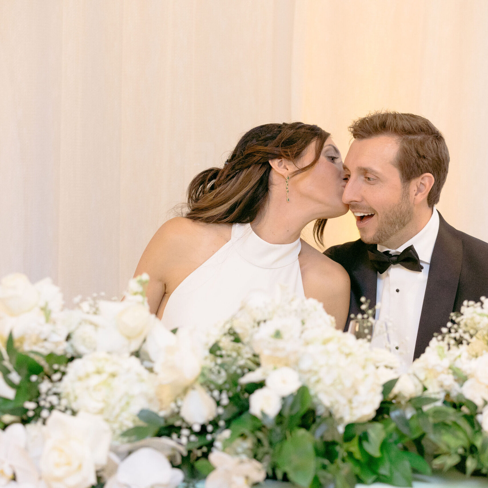 A bride and groom kissing in front of white flowers.