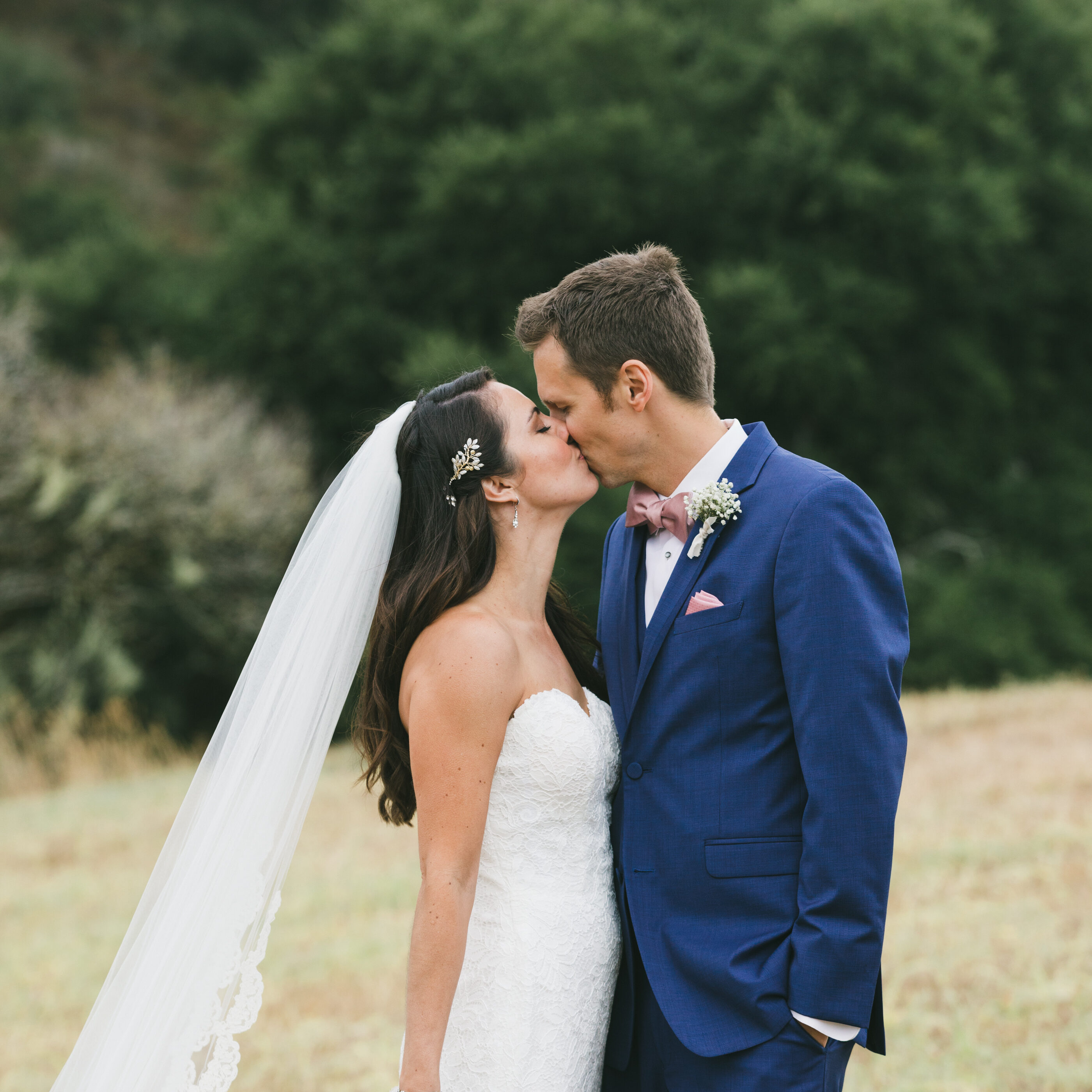 A bride and groom kissing in the grass.