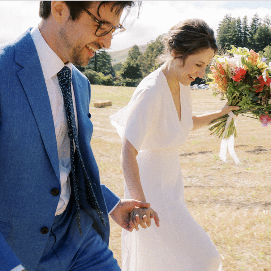 A man and woman walking through the grass holding flowers.