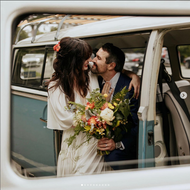 A man and woman kissing in the doorway of an old van.
